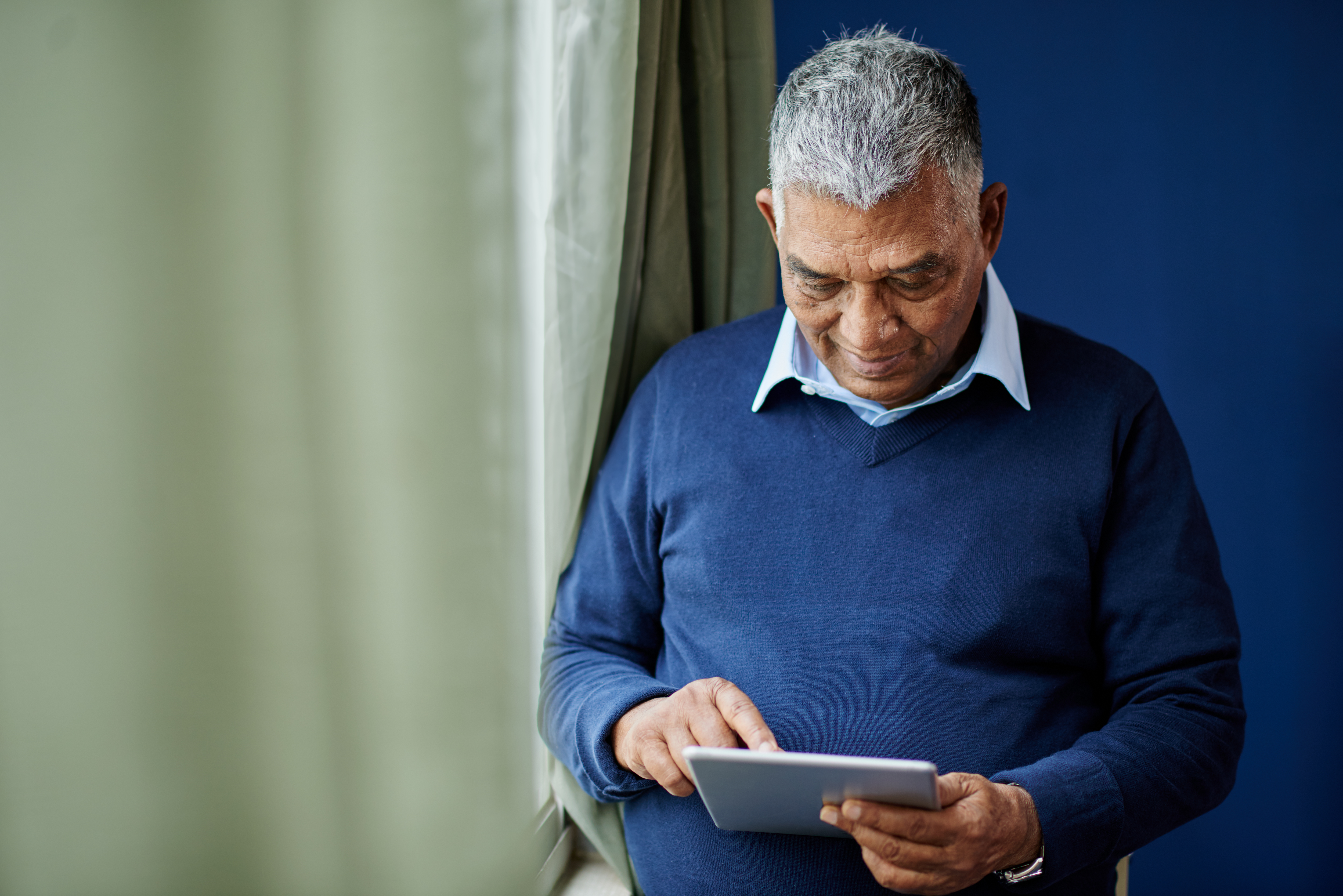 Elderly man on a iPad standing by a window