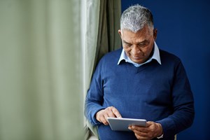 Elderly man on a iPad standing by a window